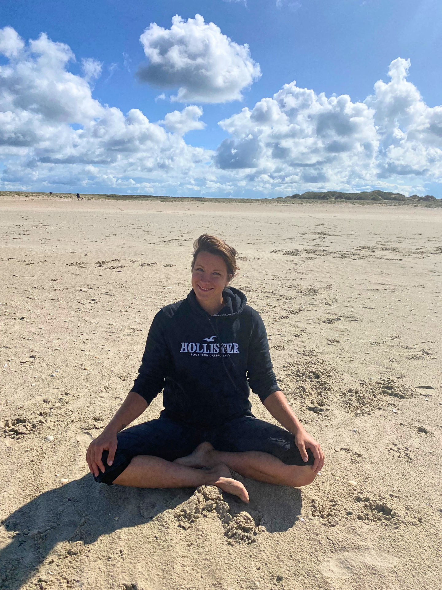 Julia sitzt am weiten Strand unter offenem Himmel